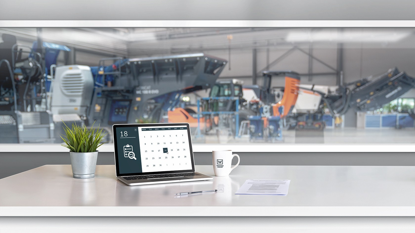 Laptop with open calendar in the foreground, blurred view of the workshop in the background