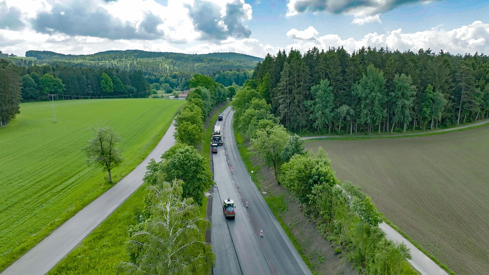 Hamm Walzen verdichten eine Asphaltstraße inmitten grüner Landschaft