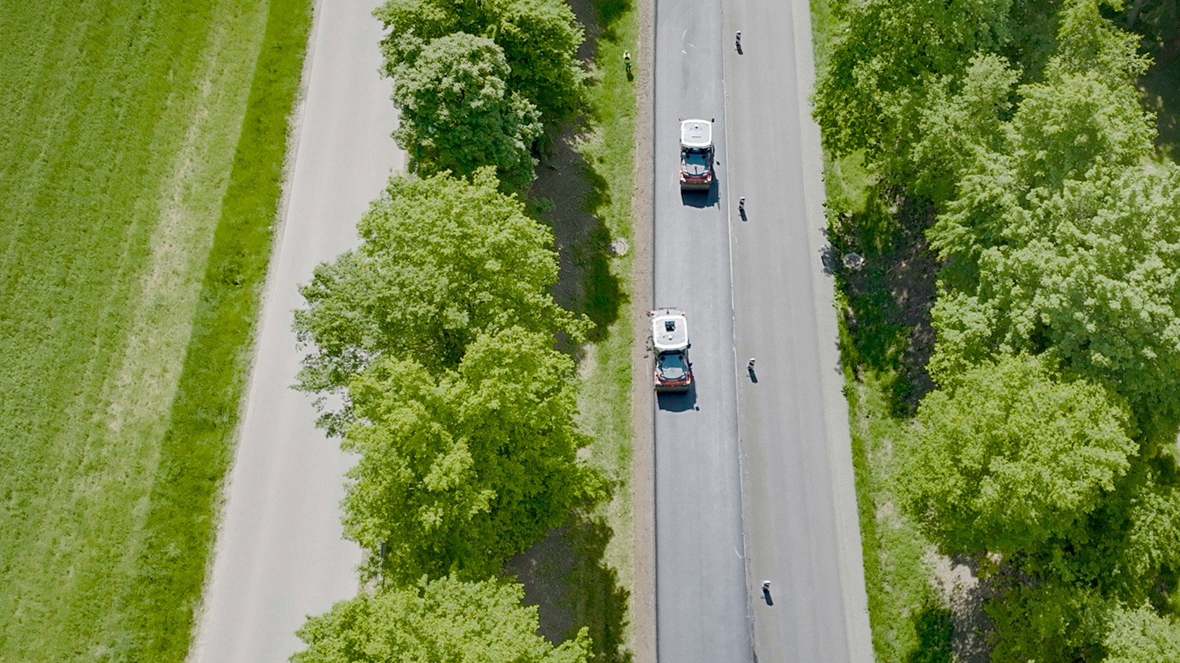 Zwei Straßenwalzen der Serie HX verdichten eine Straße inmitten grüner Landschaft