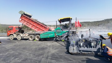The paver’s material hopper is filled from tipper trucks